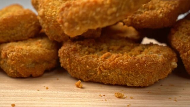 A hand picking up a crispy fried chicken nugget from a rustic wooden serving board close up shot