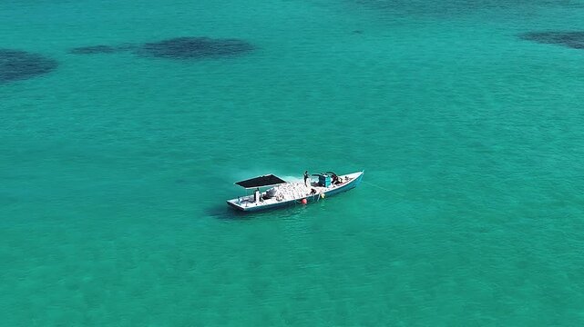 Aerial view of a traditional boat with people on board floating on the turquoise tropical waters and coral reefs in Vashafaru, Haa Alif, Maldives.
