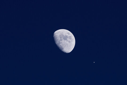 Waxing gibbous Moon and planet Venus on a daylight blue sky.