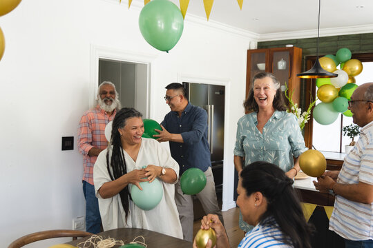 Six guests doing party planning, arranging green-gold balloons in kitchen, AR guide showing garland