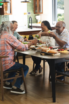 Diverse friends sharing meal at home dining table with white wine bottle, loaf of bread, salads