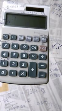 Vertical video: Camera pulling back from keypad, revealing grey calculator and algebra notes