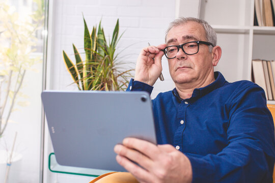 elderly man has difficulty reading a document on a digital tablet while wearing glasses.