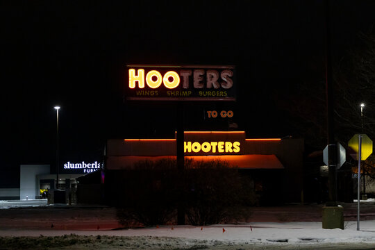 Rockford, Illinois, USA - March 12, 2026: A closed Hooters restaurant building sits empty in the dark with half of its sign lights turned off on the pole.
