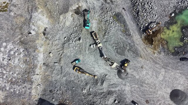 Workers use heavy machinery in a granite quarry to extract stone materials from the ground. The equipment is busy and the site is active during the day.