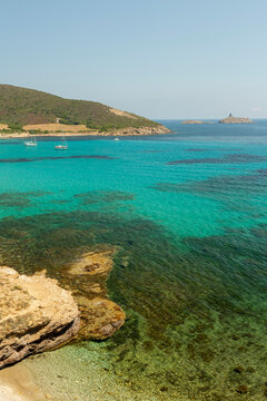 Turquoise sea with sailboats anchored near a rocky coast under a clear sky, revealing clear water and distant islands, ideal for travel, tourism, and relaxation in North Corsica, with copy space.