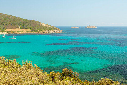 Turquoise sea and sailboats anchored in a tranquil Mediterranean bay with lush green hills and distant islands, a perfect travel and tourism destination in North Corsica.