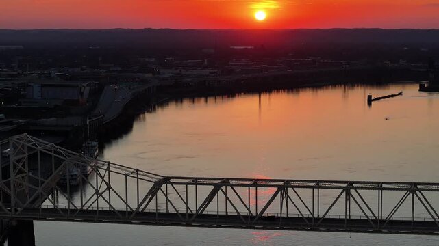 Aerial view of a large truss bridge spanning the Ohio River during a vibrant orange sunset with the city skyline in the background Louisville, Kentucky, United States.