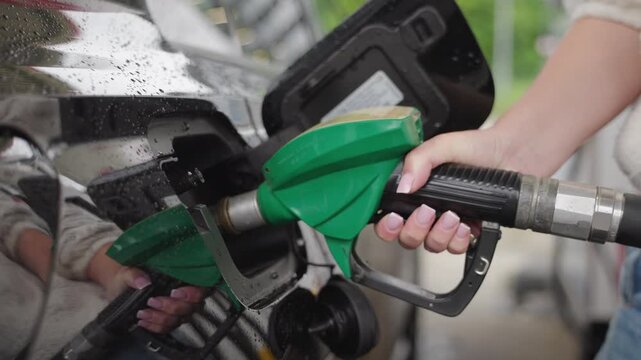 Close up of woman hand refueling black car with green fuel nozzle at gas station