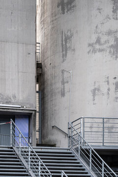Concrete facade holds stairs and railing against industrial architecture, where wall texture, geometry and shadow frame exterior access