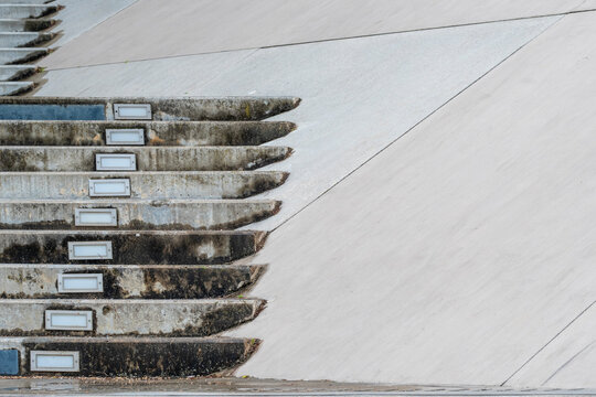 Concrete stairs meet a sloped wall in minimalist architecture, where texture, geometry, railing and shadow shape exterior access across empty design