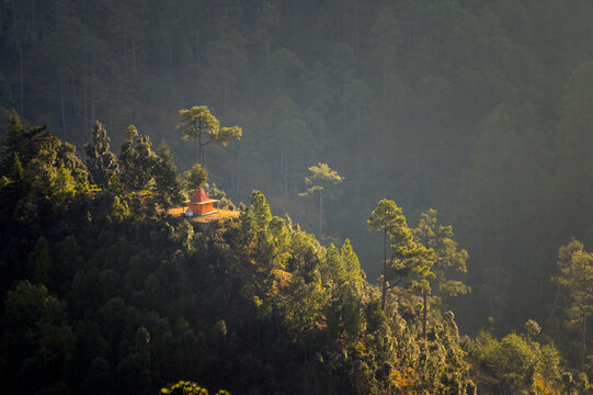 Early Morning Sun Rays Lighting a Small Remote Temple on a Forested Ridge in Pokhari Village, Ranikhet, Uttarakhand, India