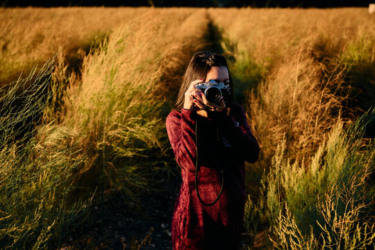 Woman shooting with a vintage camera in a golden field