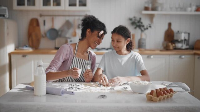 Master class for teen girl how to make homemade cookies, african woman and girl. Housewife teaching her daughter to cook and bake, happy smiling people in cozy home kitchen interior, medium shot