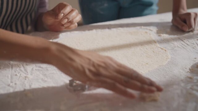 Housewife and her daughter cutting figured cookies from raw dough, closeup view. Homemade bakery for fest, inside home kitchen, mother and child spending time together in vacation, cooking and baking