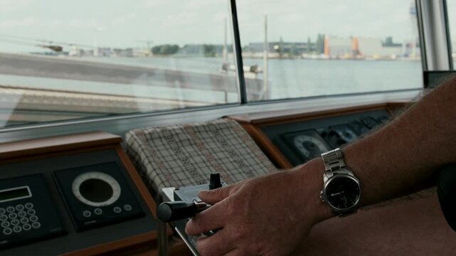 Man's hand operating the helm and navigation controls of a ship navigating the port of Amsterdam