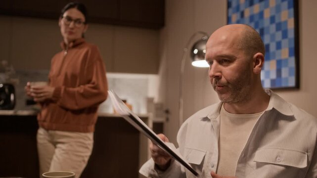 Close up of angry man singing divorce agreement and giving it to woman who drinking coffee in background