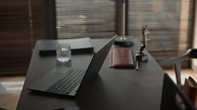 Pull out shot of black laptop on wooden table in spacious lawyers office fully equipped with furniture
