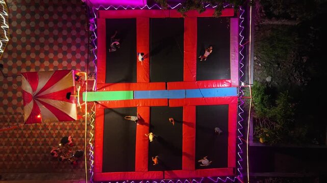 Aerial view of people jumping on colorful trampolines at GOR Gelarsena Klaten Night Market with neon lights at night Kecamatan Klaten Utara, Jawa Tengah, Indonesia.