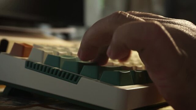 A close up profile shot of a single male hand slowly operating a mechanical keyboard, highlighted by warm golden sunlight that casts soft shadows over the green and white keycaps.