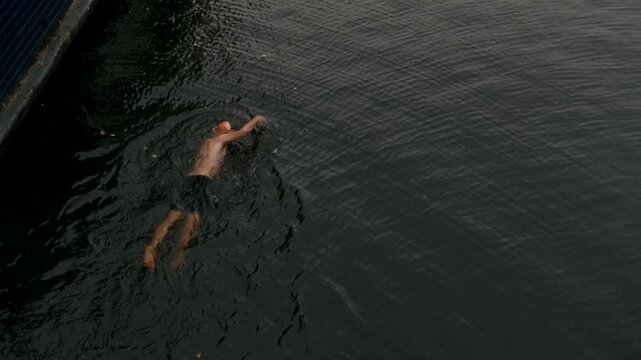 Athletic man swimming backstroke in a city canal between houseboats in Amsterdam