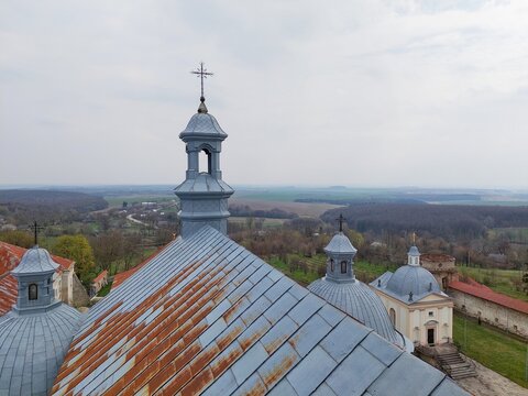 A high-angle shot showcasing the historic Dominican Monastery in Pidkamin, Lviv region, Ukraine. The image features the intricate Baroque architecture, rusted metal roofs of the cathedral, and stone 