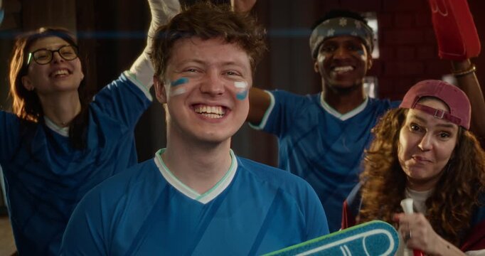 Portrait shot of group of enthusiastic fans dressed blue uniforms, with face paint and team gear, celebrating their teams victory at bar