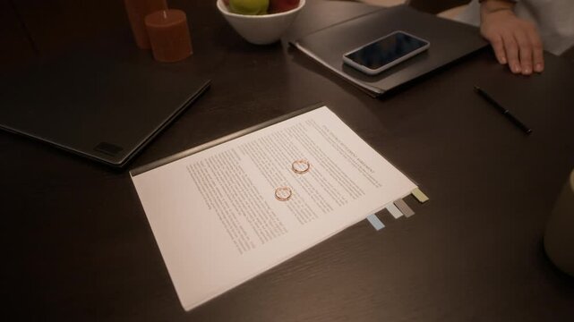 Close up shot of anonymous ex spouses putting their wedding rings on divorce agreement placed on dining table in kitchen at home