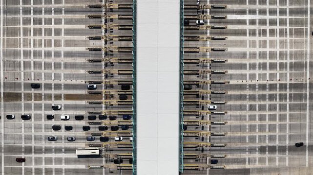 Overhead drone view showing cars queuing and driving through a busy toll plaza on a multi-lane highway, representing transportation infrastructure, commuting, and modern road systems