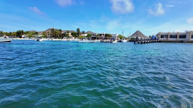 POV from a stationary boat with a slow panning view of Gran Roque island, sailing in the calm Caribbean Sea, and tropical coastline in the Los Roques archipelago, Venezuela, under bright sun.