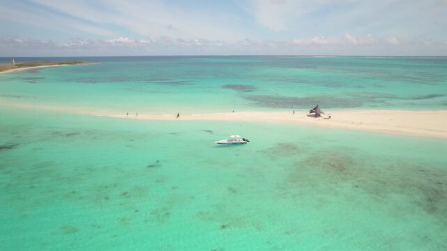 Aerial zoom out revealing tropical sandbar at Cayo de Agua in Los Roques Archipelago Venezuela with people, yacht and beach tent surrounded by turquoise Caribbean waters in a remote island
