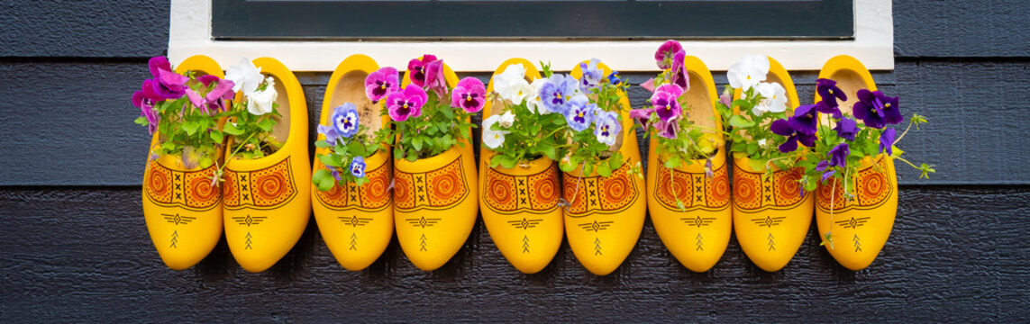 Old wooden Dutch shoes - klomps. A lot of colorful old clomps against the background of a wooden wall. Popular souvenirs. Traditions of Holland. Background