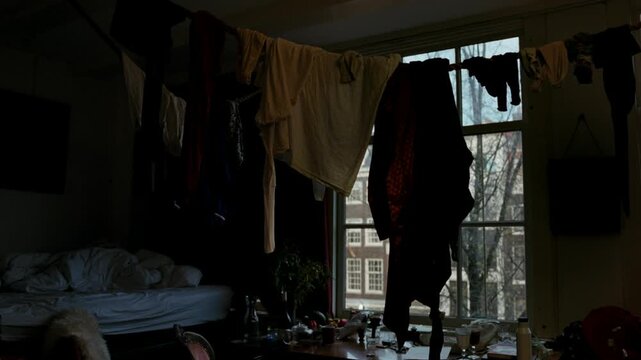 Disorganized and cluttered student room with an unmade bed and clothes drying on a clothesline