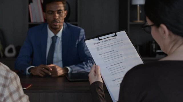 Over shoulder view of unrecognizable couple listening to lawyer while he talking about documents, settlement agreement and divorce process overview