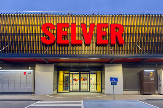 Tallinn, Harju Estonia - 12.05.2026: Modern Selver supermarket facade in the evening with large red illuminated sign, yellow slatted wall, glass entrance and parcel lockers DPD, UPS, Venipak.