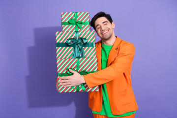 Naklejka premium Happy man holding stack of wrapped Christmas gifts in colorful outfit against purple background