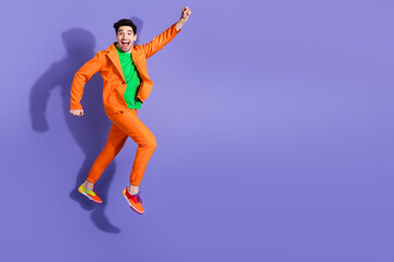 Obraz premium Happy man jumping in an orange suit against a purple background celebrating playful colorful fashion and energetic movement for lifestyle and advertising photography
