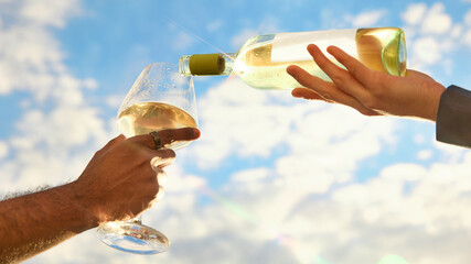 Obraz premium White wine pouring into glass against bright blue summer sky. Concept of winery promo, summer aperitif, outdoor celebration, elegant tasting, and premium beverage advertising.