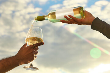 Obraz premium White wine pouring into glass against bright sky with sun flare. Concept of premium winery promo, summer aperitif, outdoor celebration, restaurant menu and luxury travel.