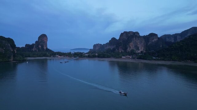 Krabi, Thailand : Aerial drone footage of traditional long tail boat leaves jetty in Railay east side in coastline of Krabi, Thailand surrounded by limestone cliff before sunrise