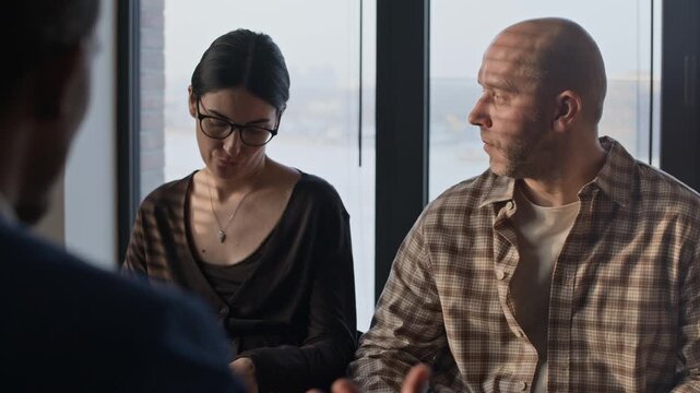 Over shoulder view of two spouses sitting in chairs and listening to lawyers speech during divorce consultation