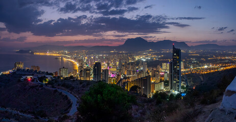 Obraz premium City lights of Benidorm after sunset. Sky purple and silhouettes of mountains at background.