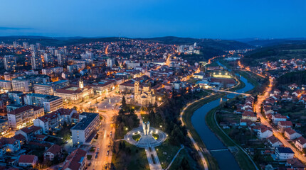 Obraz premium Aerial view of a city at dusk with a river winding through it and illuminated buildings.