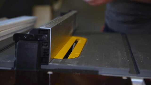 Circular table saw cutting wood in carpenter workshop close up. A running blade on a bench saw sawing trough the wooden log in the middle of a working space, close up footage. A sawing circle that cut