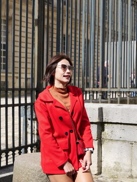 A woman wearing a red jacket and sunglasses stands in front of a metal fence
