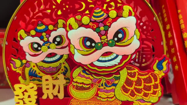 Bright red and gold Chinese lion dance ornaments displayed as festive decorations for Lunar New Year celebration. Traditional Asian cultural symbols with vibrant colors and glitter details.