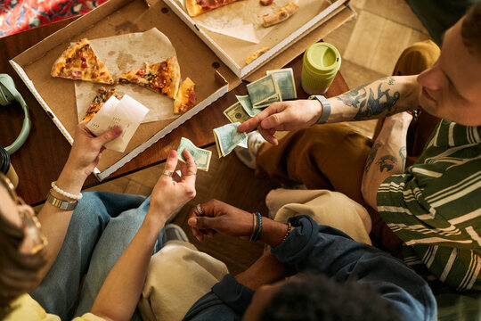 Overhead view of multiethnic young adults splitting cash and checking receipt over shared pizza, showing group expense sharing and casual budgeting. Useful for payment apps or cost sharing ads