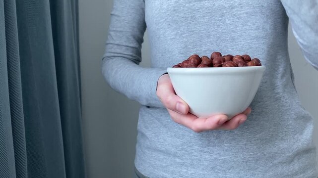A woman takes a hazelnut from a plate. Snacking during the day. Choosing a healthy alternative to sweets or fast food. Nuts are a convenient and nutritious option for quick energy replenishment