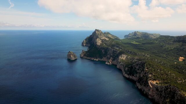 Aerial view of the rugged limestone cliffs and deep blue sea at Cap de Formentor with green hills under a cloudy sky, Balearic Islands, Balearic Islands, Spain.