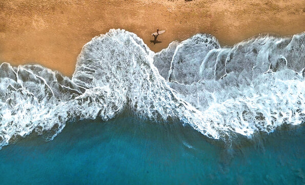 AERIAL, TOP DOWN: Unrecognizable surfer walking along the exotic sandy beach.